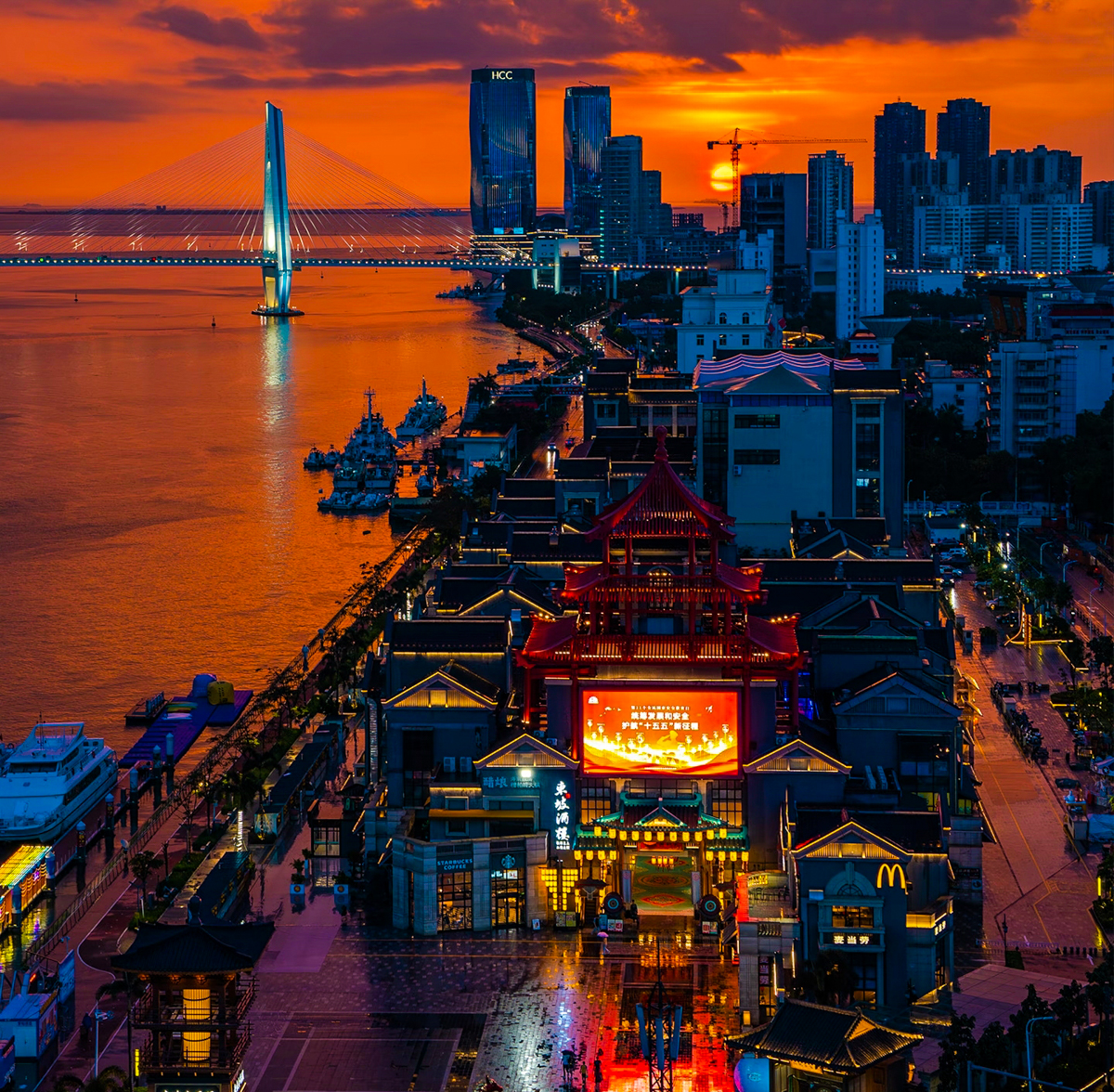 海口滨海大道与城市天际线在傍晚时分的景色，椰子树沿路排列，落日把海面染成温暖的橘金色