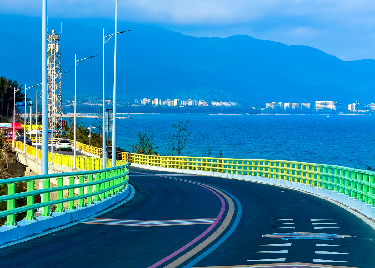 万宁滨海旅游公路沿线的海湾与礁石景观，蓝色海浪拍打海岸，公路贴着海平线向远处延伸